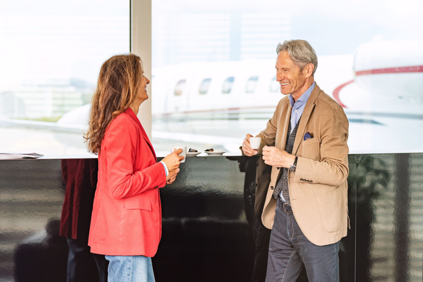 couple having coffee standing in an airport terminal, parked aircraft in the background